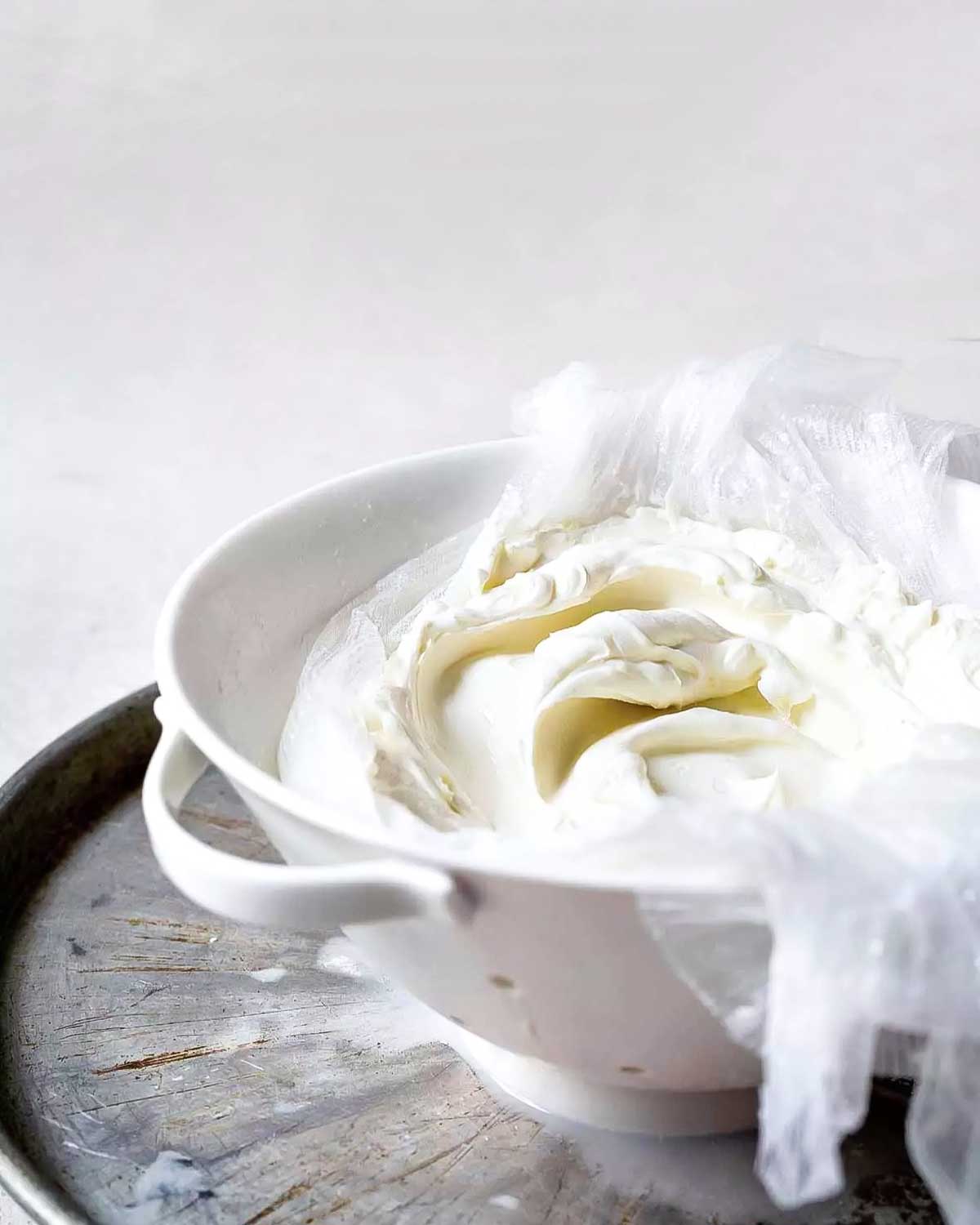 A strainer filled with homemade yogurt with cheesecloth on top.