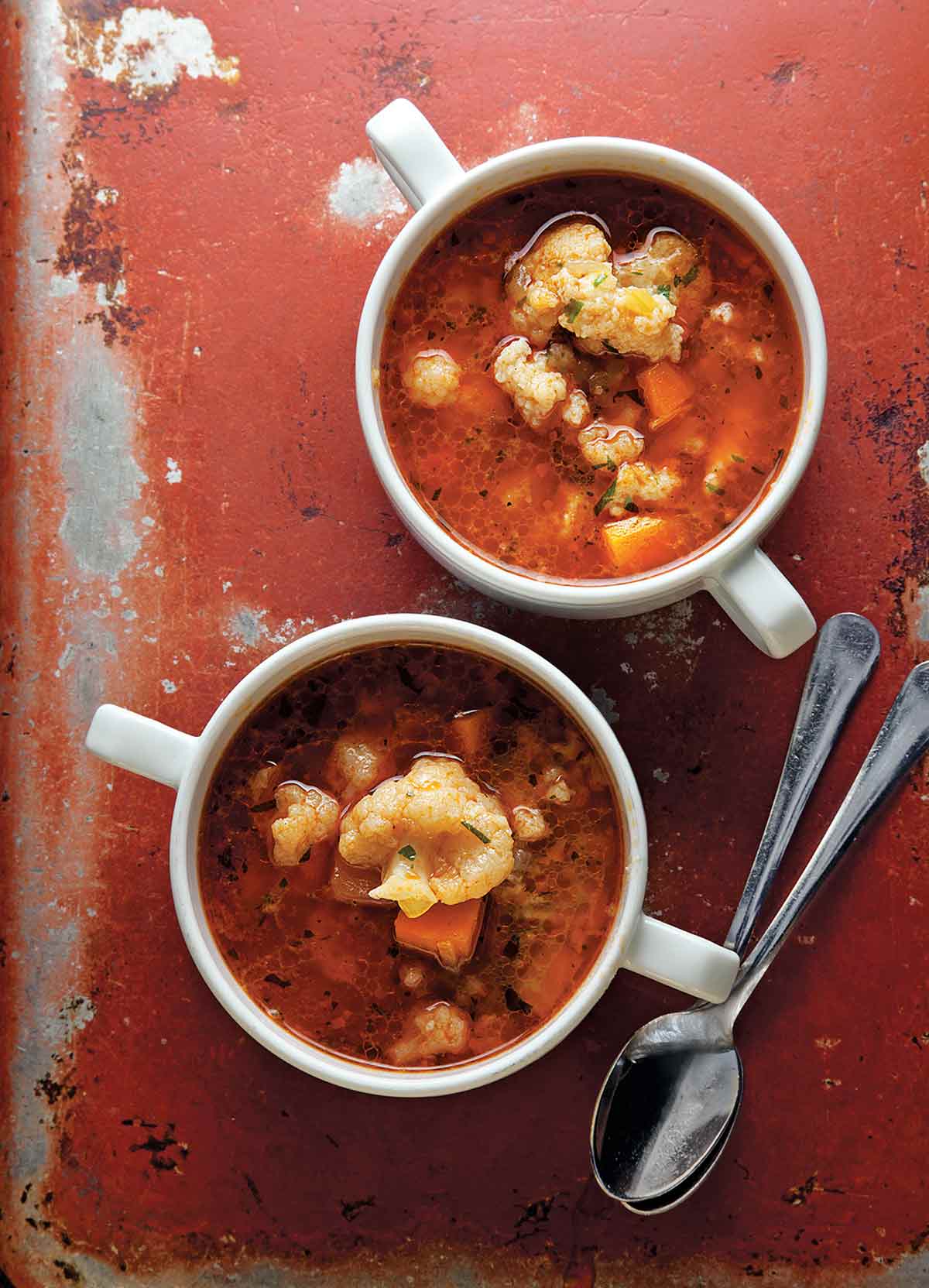 Two mugs of Hungarian cauliflower soup with two spoons beside them.