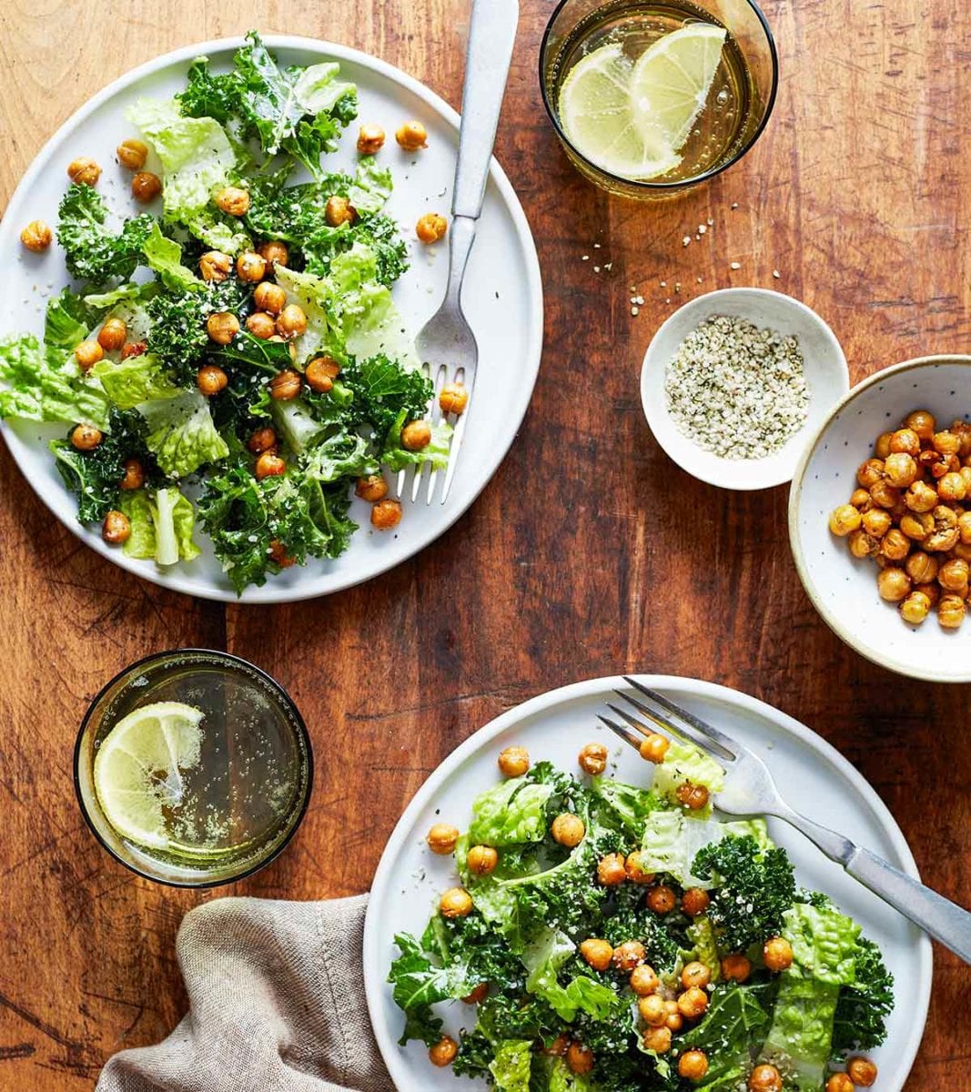 Two plates topped with kale caesar salad with roasted chickpeas on top and in a dish on the side.