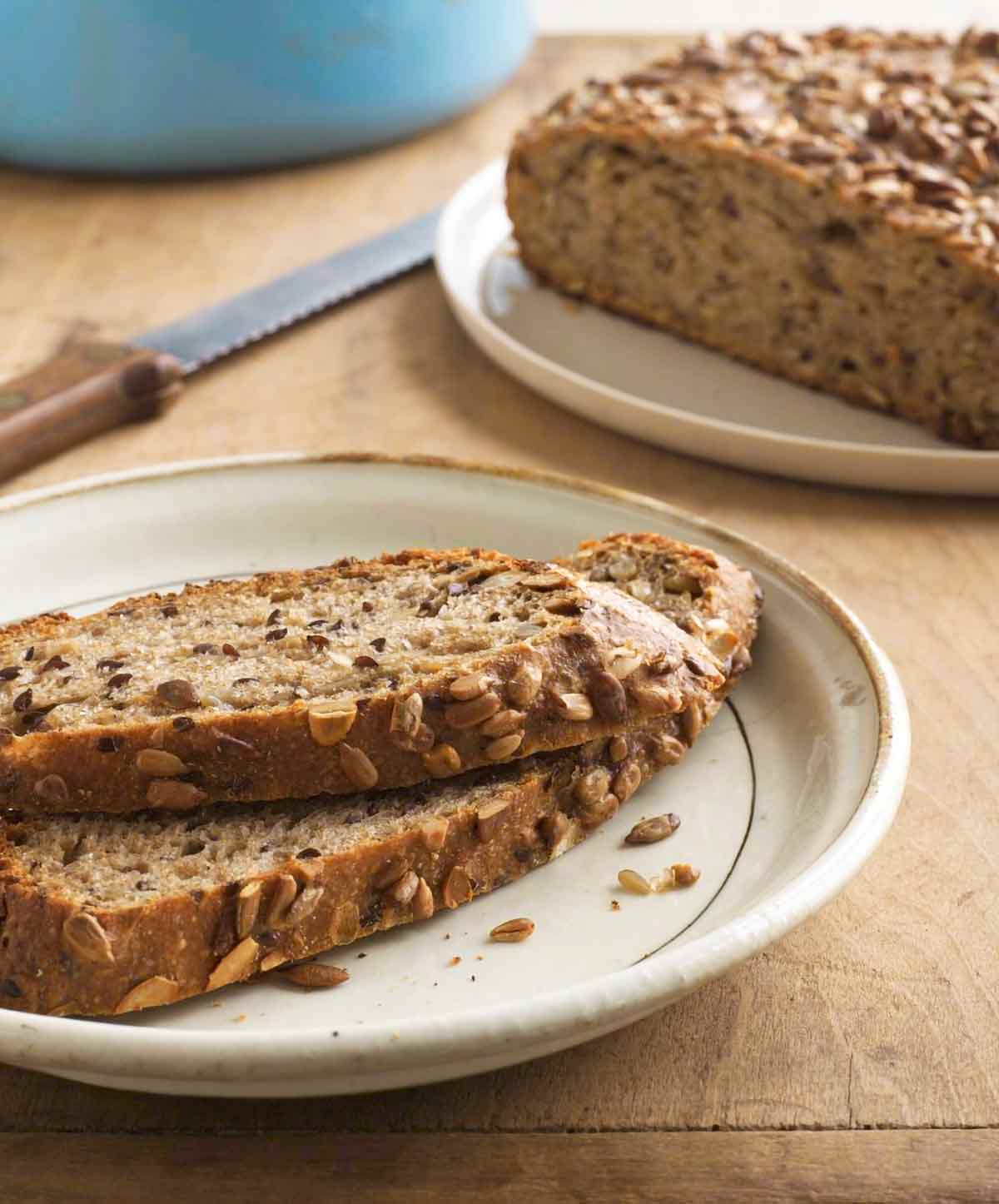 Two slices of no-knead pumpkin-sunflower seed bread on a white plate with the remaining loaf next to it on a separate plate.