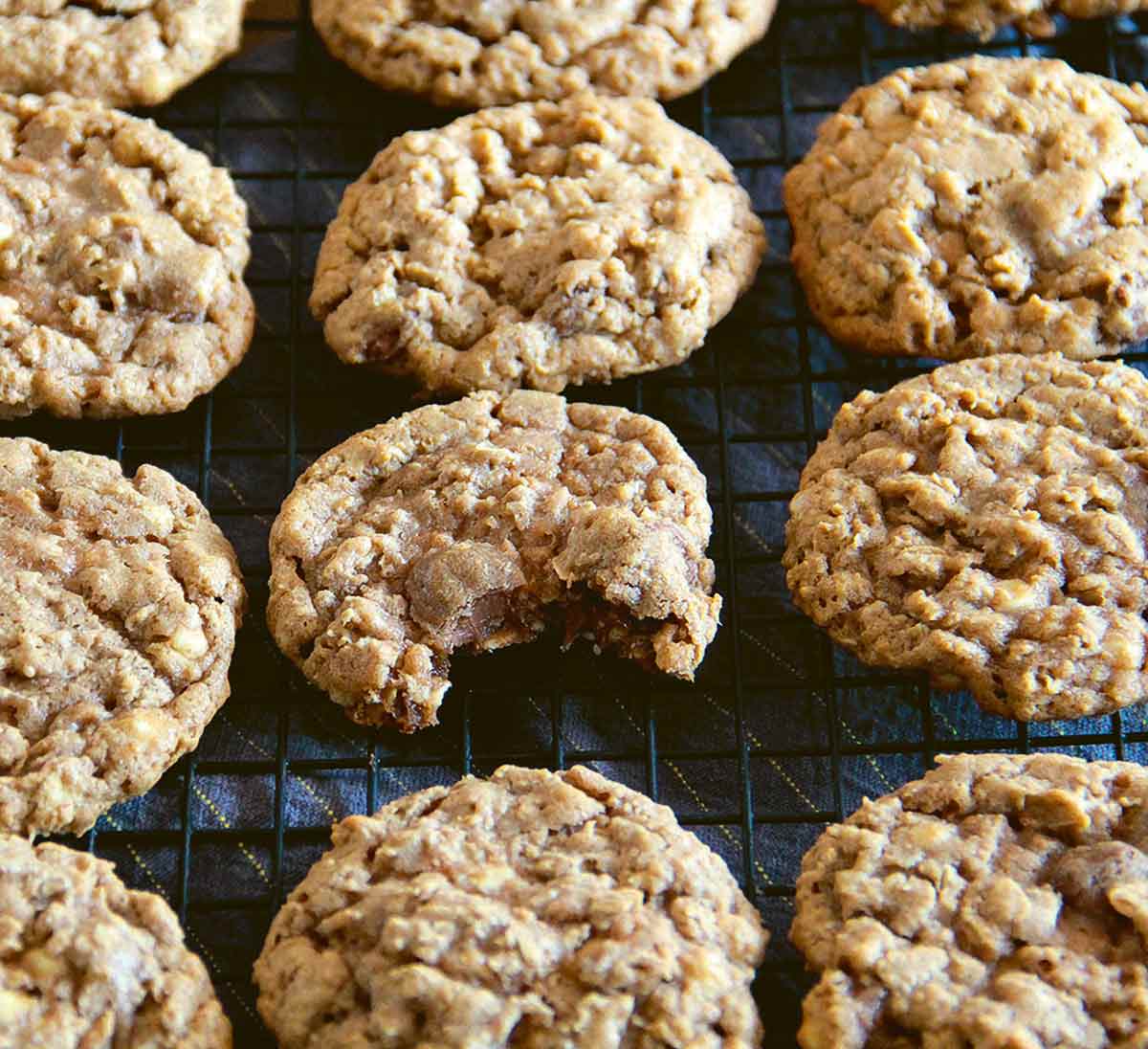 Several oatmeal chocolate chip cookies cooling on a rack, one with a bite out of it.