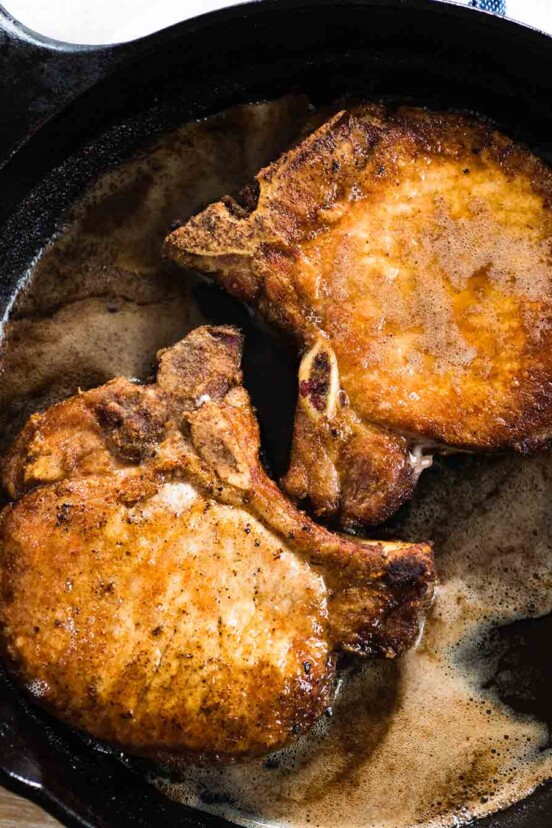 Two golden pan-fried pork chops in a cast-iron skillet.