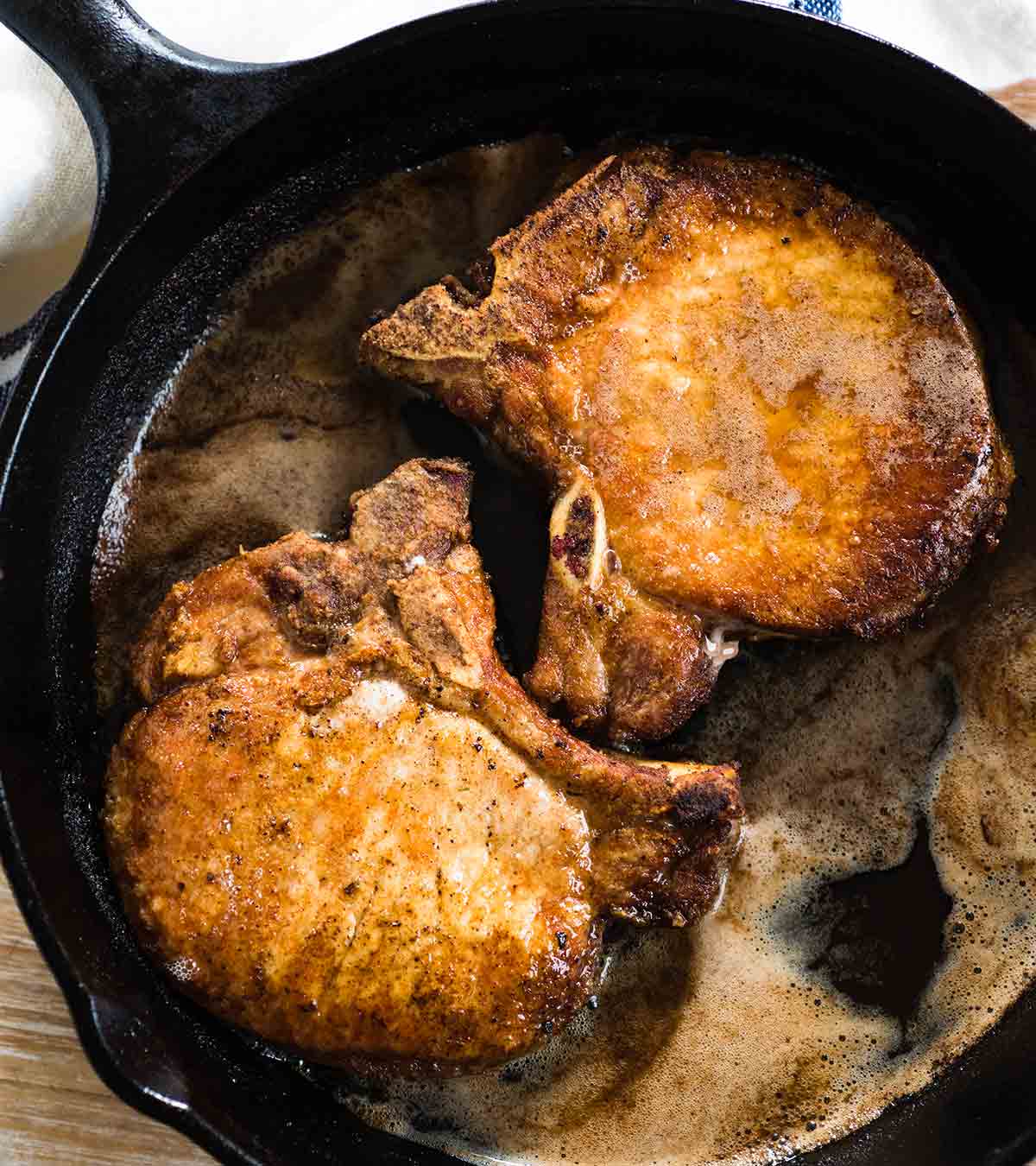 Two golden pan-fried pork chops in a cast-iron skillet.