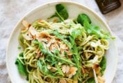 A bowl of pasta with avocado sauce, toasted flaked almonds and a handful of arugula on top.