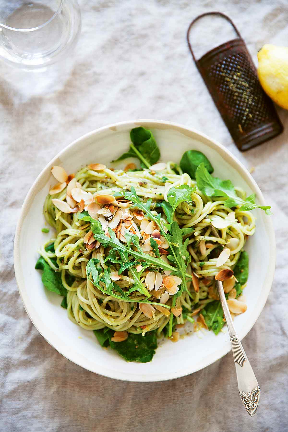 A bowl of pasta with avocado sauce, toasted flaked almonds and a handful of arugula on top.