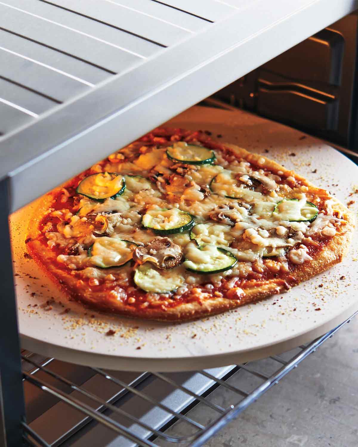 A cooked pizza on a pizza stone coming out of an oven.