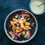A white bowl filled with roasted kabocha squash, black rice, and sesame dressing drizzled over and in a glass on the side.
