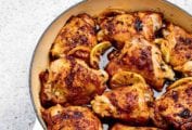 Nine roast lemon chicken thighs in a round Dutch oven with lemon slices tucked between them.