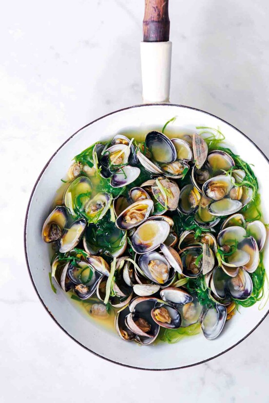 A white enamel wok filled with sake-steamed clams, broth, and scallions.