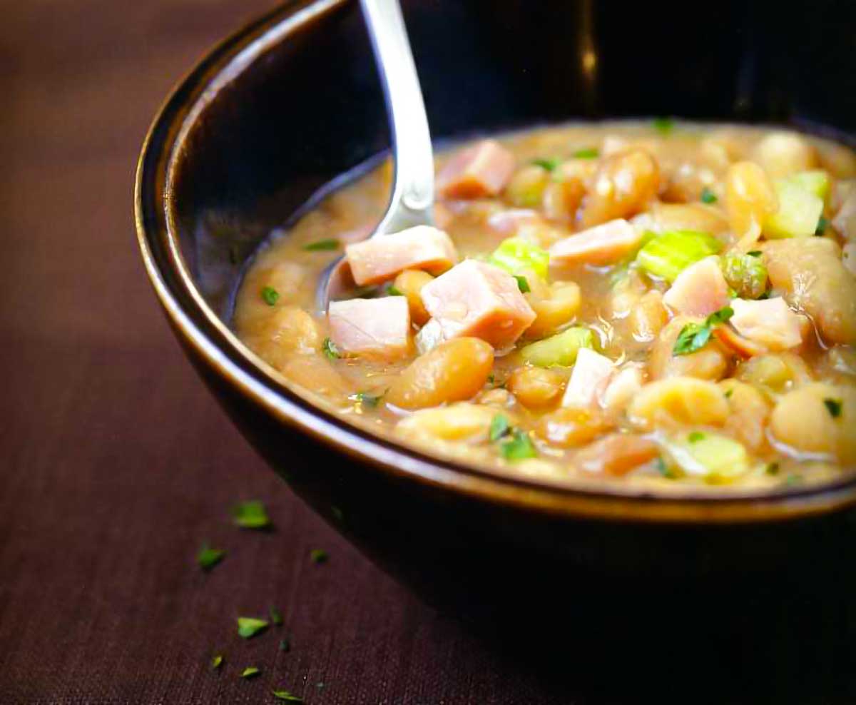 A brown bowl half-filled with senate bean soup with a spoon resting inside the bowl.