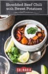 A bowl of shredded beef chili with sweet potatoes on a plate with lime wedges and cilantro.