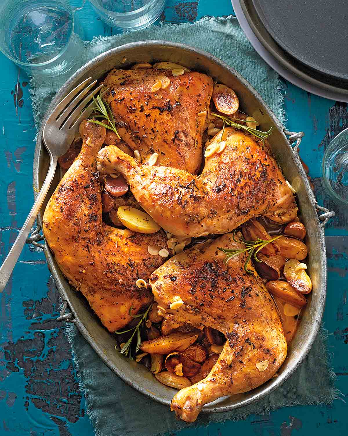 An oval dish filled with slow cooker chicken with garlic and potatoes and sprigs of rosemary with a fork nestled inside.