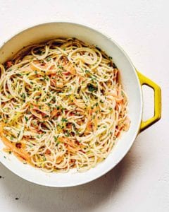 A yellow and white pot filled with smoked salmon pasta and garnished with fresh chives.
