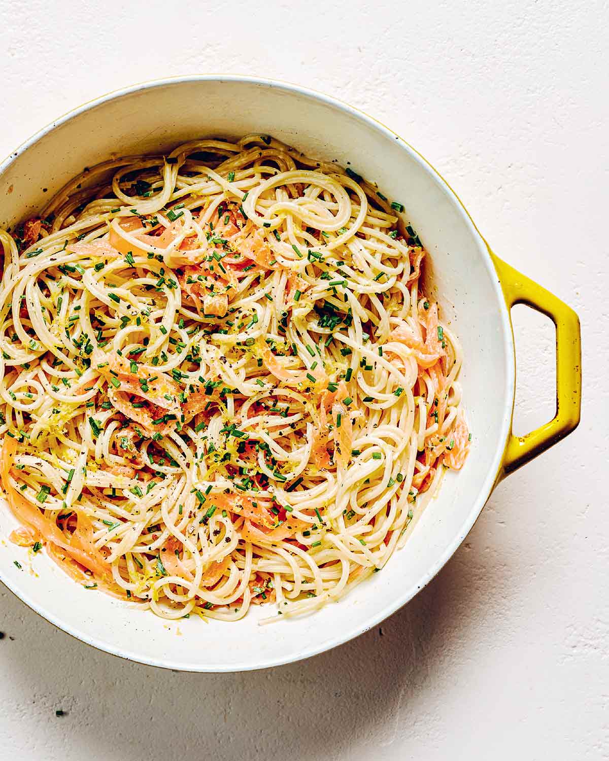 A yellow and white pot filled with smoked salmon pasta and garnished with fresh chives.