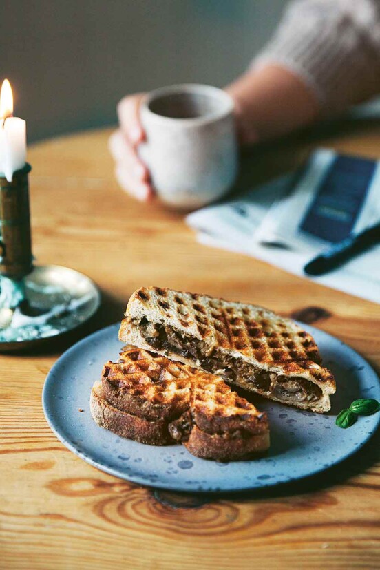 Two halves of waffle toasties with mushrooms on a blue plate with a candle beside it an a person in the background.