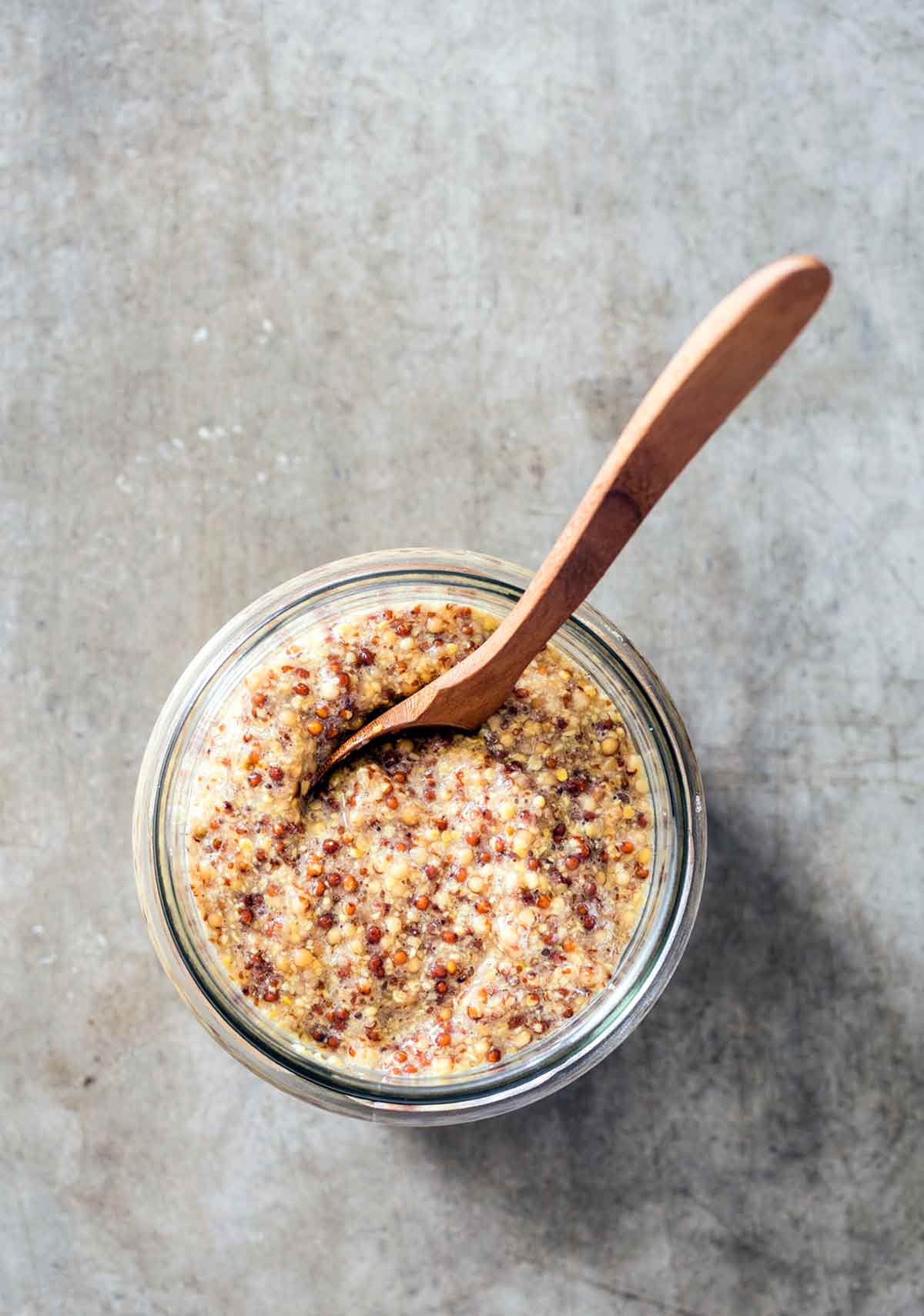 A jar of whole grain mustard with a wooden spoon in it.