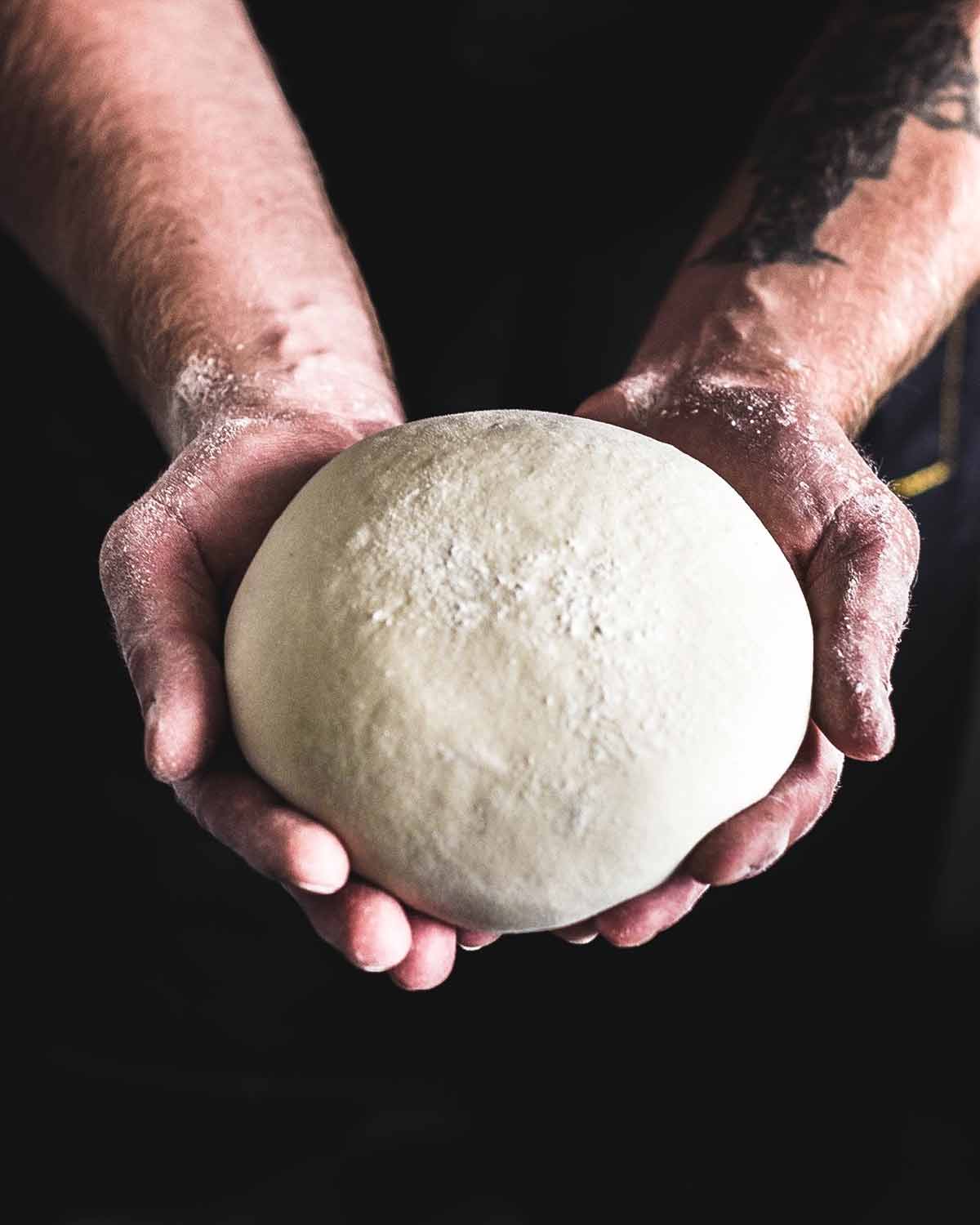 A person holding a ball of pizza dough.