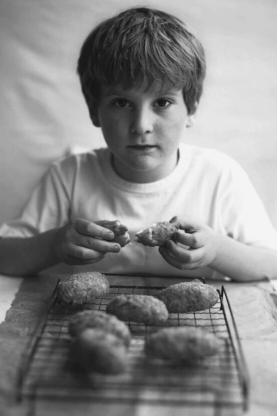 A boy opening an arancini with six more cooling on a rack in front of him.