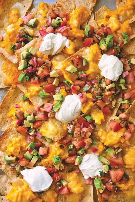 A pile of breakfast nachos topped with cheese, eggs, salsa, and sour cream on a baking sheet.