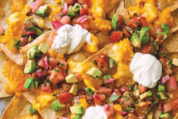 A pile of breakfast nachos topped with cheese, eggs, salsa, and sour cream on a baking sheet.