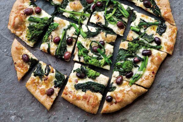 A broccoli rabe pizza cut into squares on a grey background.