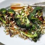 A white oval plate topped with broccoli with walnuts, raisins, and ricotta salata with a fork and spoon on the side.
