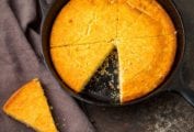 Cheddar cornbread in a cast-iron skillet, cut into 8 wedges, with one wedge removed.