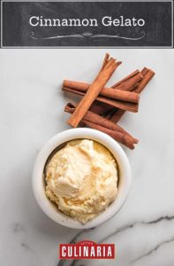 A small bowl of cinnamon gelato with cinnamon sticks next to it on white marble surface.