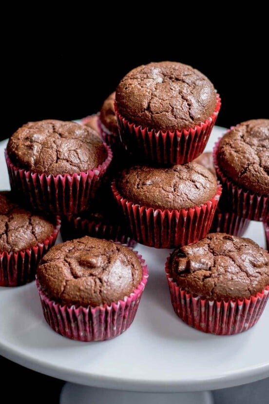 Cocoa muffins piled on top of each other on a white cake platter.