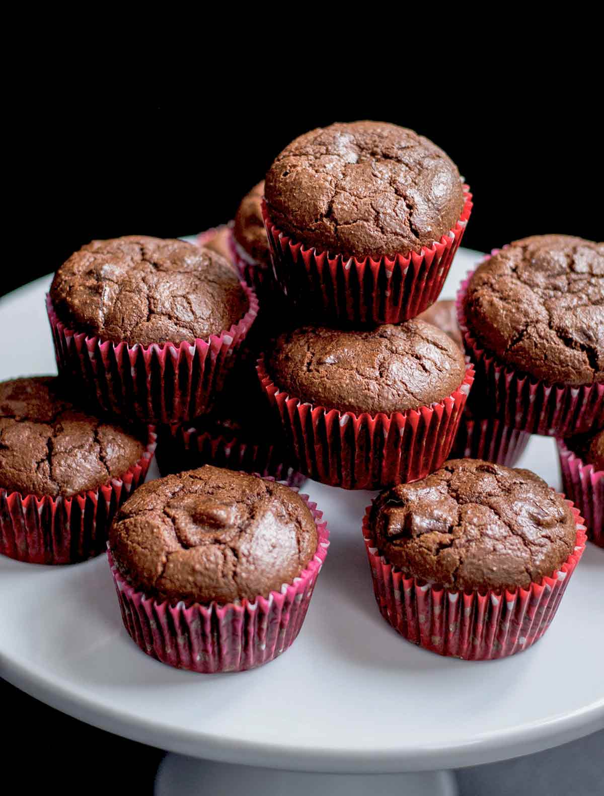 Cocoa muffins piled on top of each other on a white cake platter.