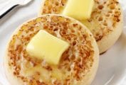 Two English crumpet on a white plate, each topped with a pat of butter.