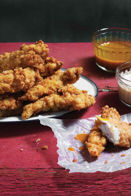 A plate piled with homemade chicken strips and dishes of dipping sauce on the side.