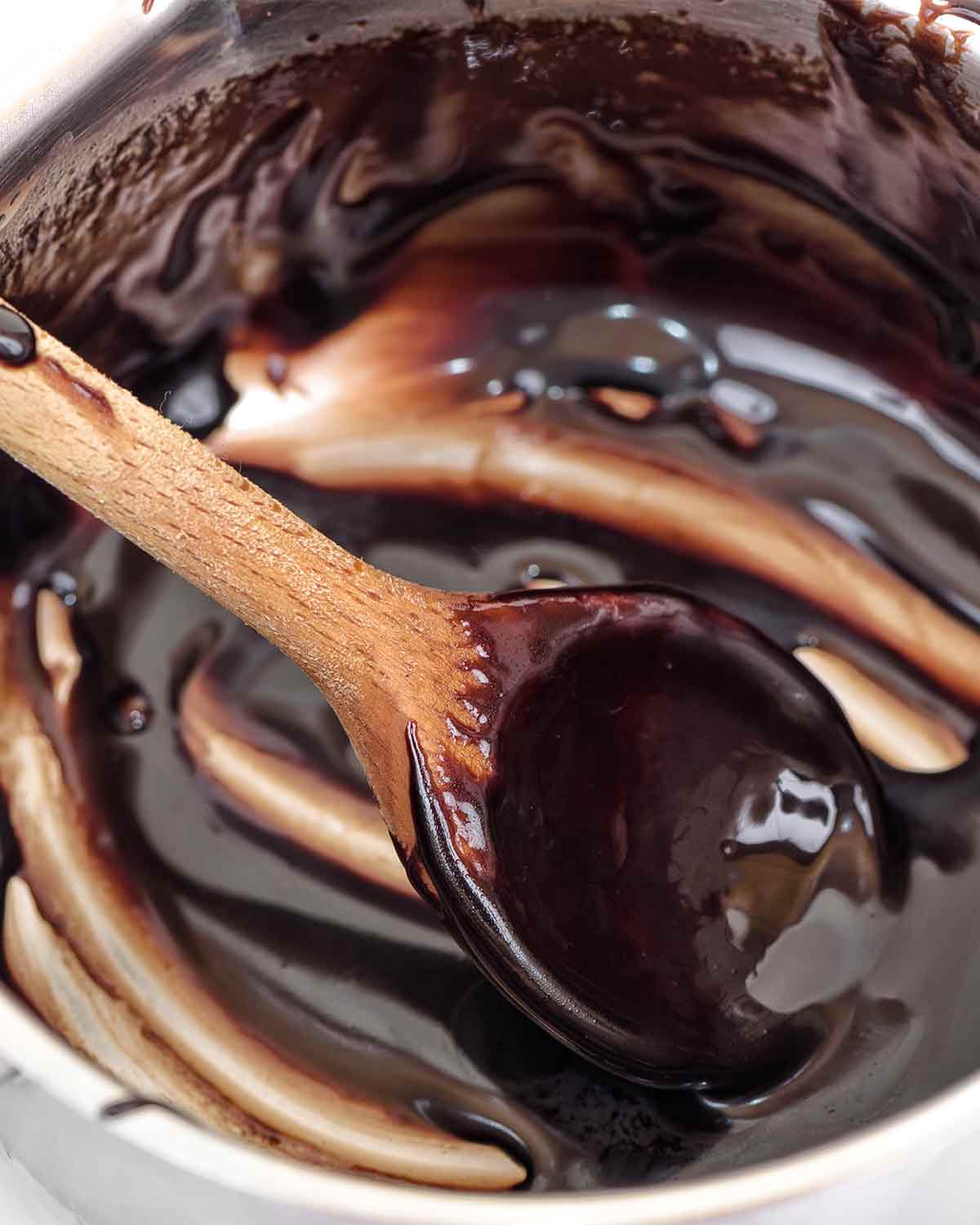 An almost empty pot with traces of hot fudge sauce and a wooden spoon resting inside.