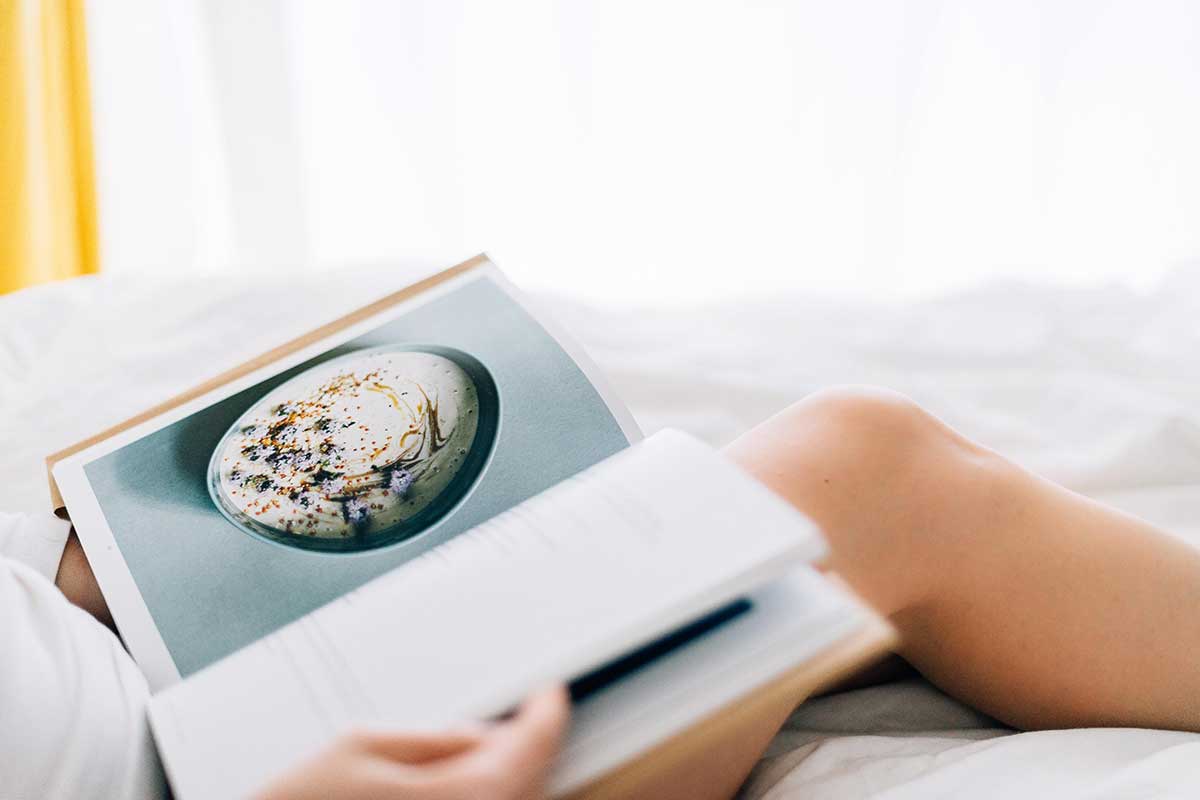 A woman reading a cookbook in bed for the podcast Talking With My Mouth Full, Ep. 40: Cookbook Author Julia Turshen on Feeding Others