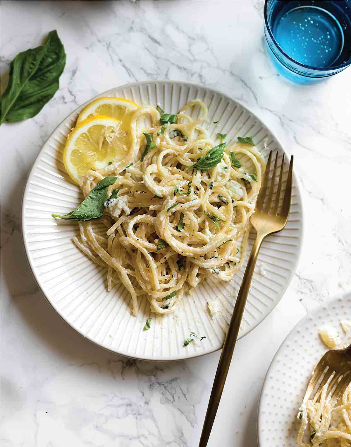 Two white plates topped with lemon basil pasta with lemon slices on the side and a gold fork resting on the side of each plate.