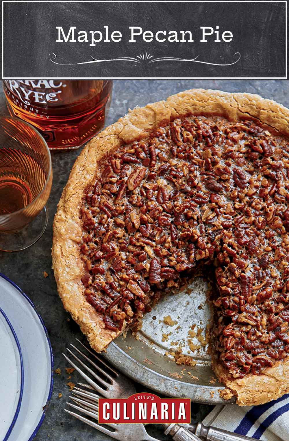 A maple pecan pie in a metal pie plate with one slice missing and forks, plates, and a bottle of rye whiskey beside the pie.