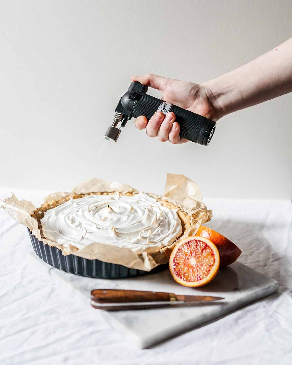 A person toasting a meringue on a tart with a torch.
