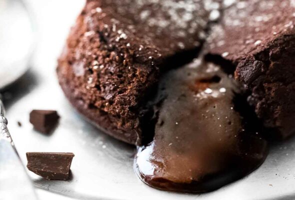 A molten chocolate cake on a plate with the filling oozing out and a few pieces of dark chocolate on the side.