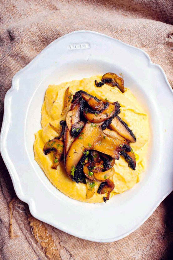 A white bowl filled with polenta with garlic and mushrooms and sage garnish.