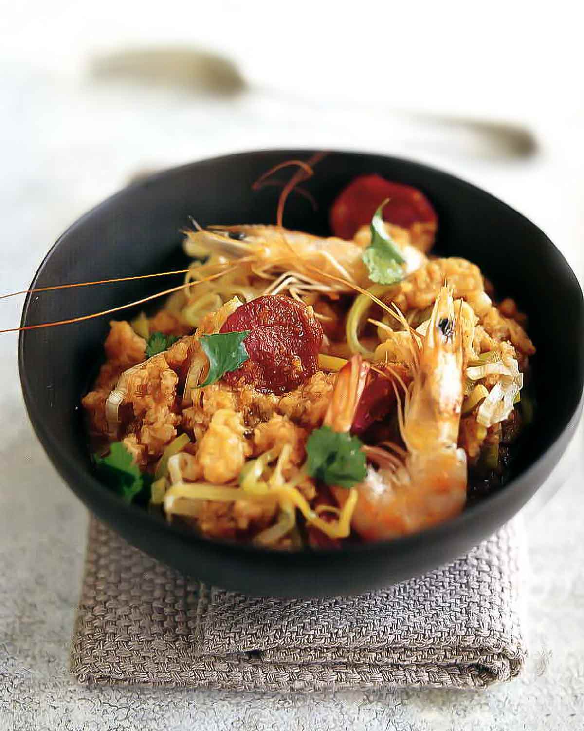 A black bowl filled with Portuguese bread soup with shrimp on a grey folded cloth.