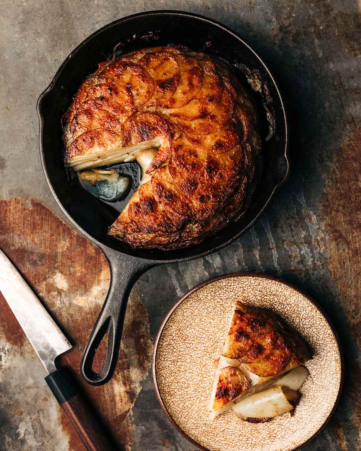 A potato galette in a cast-iron skillet with one wedge missing.