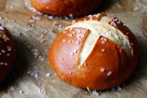 Three pretzel rolls on a sheet of parchment sprinkled with coarse salt.