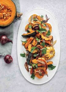 A white oval platter topped with roast winter squash and shallots.