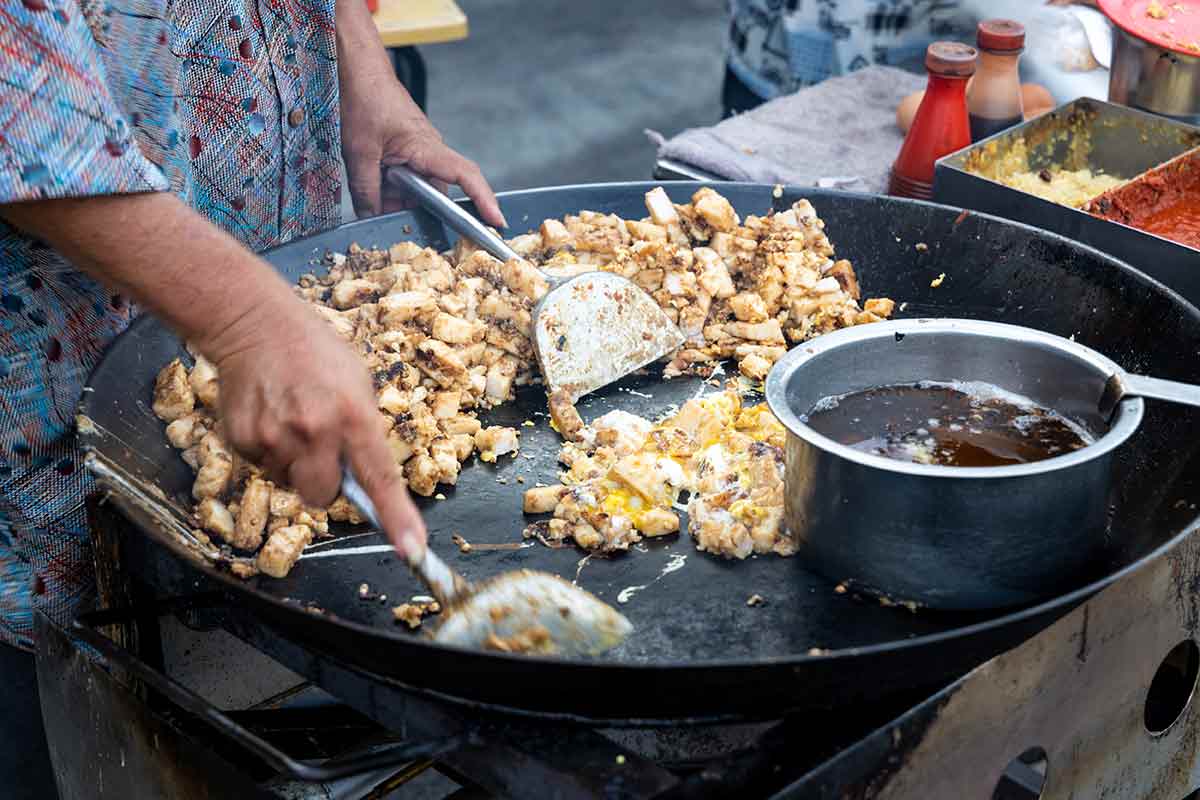 A street food vendor in Singapore stirring food on an open-air grill.