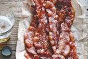 A wire basket lined with parchment and filled with sweet and spicy bacon with a glass of beer on the side.