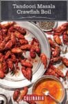 Crawfish piled on a platter and on newspaper beneath it with a bowl of butter beside for a tandoori masala crawfish boil.