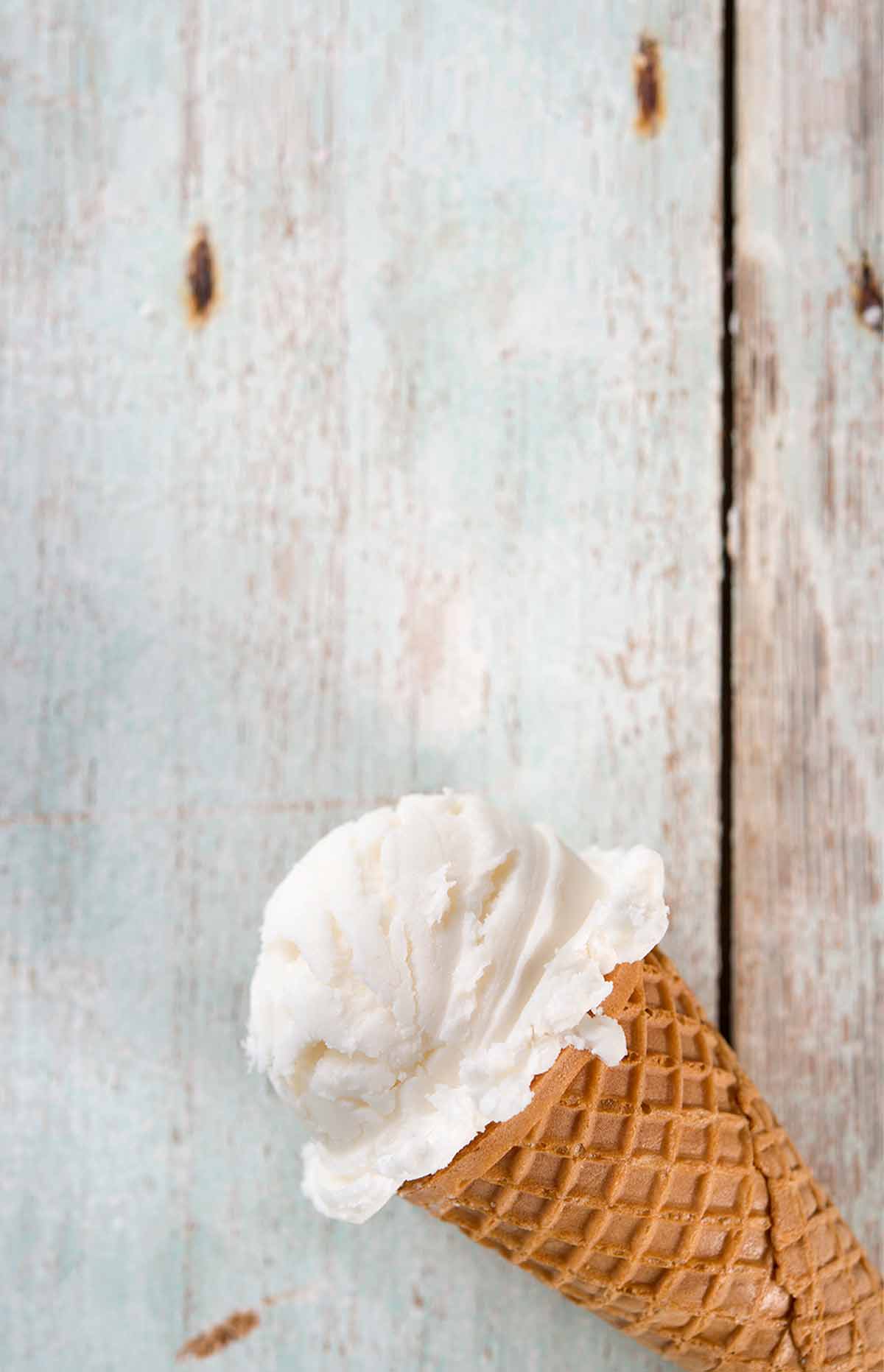 An ice cream cone with a scoop of toasted coconut ice cream on a white wood background.