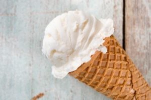 An ice cream cone with a scoop of toasted coconut ice cream on a white wood background.