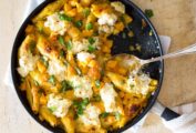 A skillet filled with unstuffed pasta shells with butternut squash on a wooden board with a spoon resting inside.