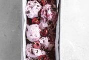 A parchment-lined metal tin filled with vegan chocolate cherry chunk ice cream and whole cherries on top.